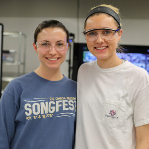 Two female students with protective eye gears smiling to the camera.