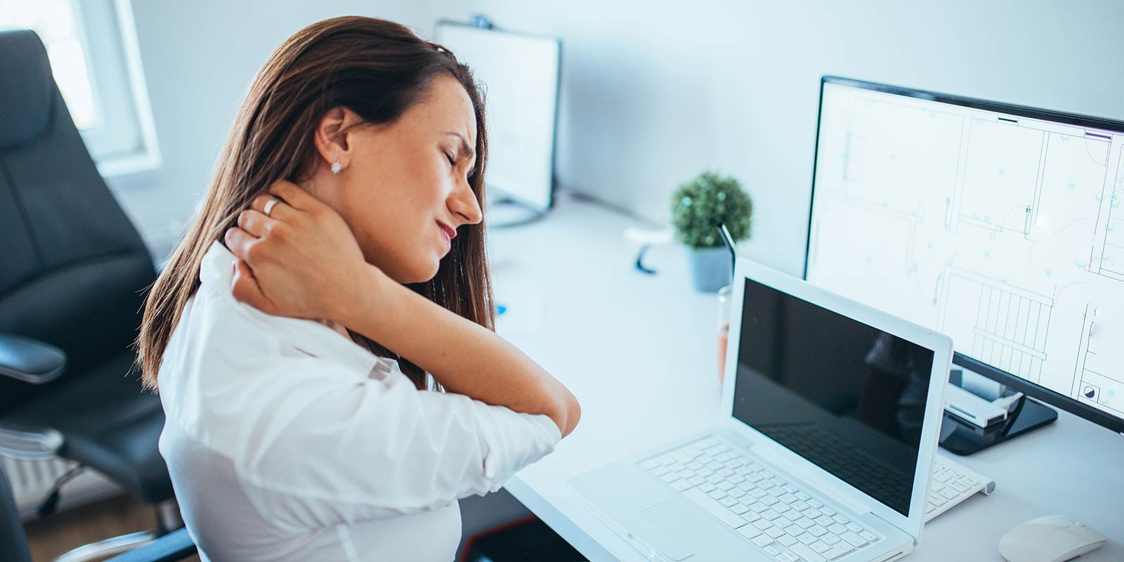 Woman in front to computer screen holds her painful neck.