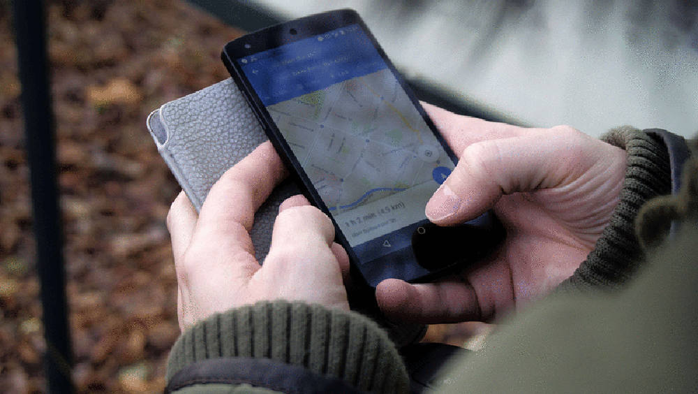 Hands holding cellphone showing map on screen and gray cellphone case