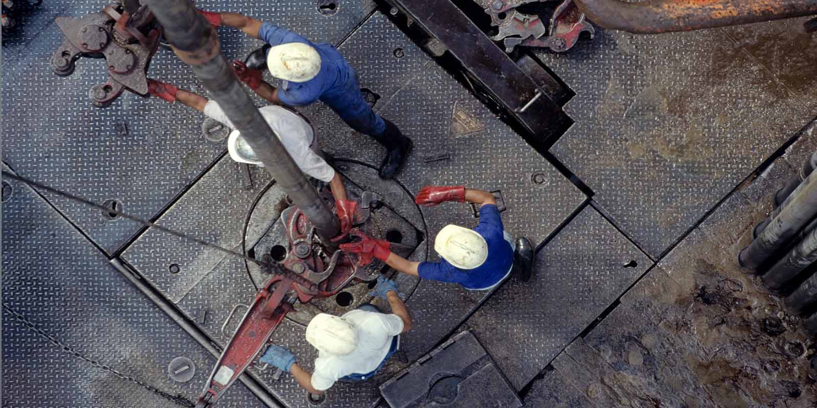 Overhead view of four workers wearing hardhats and using drilling equipment on a rig.