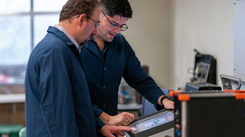 Male professor and male graduate student researcher study screen of downhole drilling simulator device