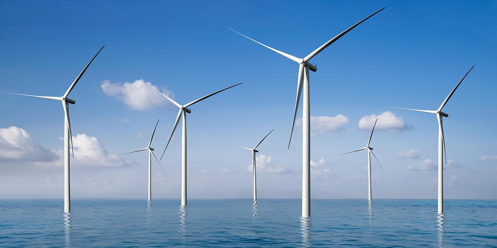 Wind turbines in the ocean are backed by a blue sky with clouds.